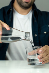 Unrecognizable man pouring water into a glass to hydrate himself - hydration and wellness concept