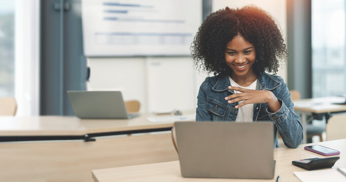 Smiling afro businesswoman in blue jeans working on laptop in modern office