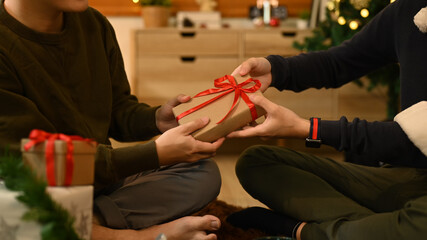 Image of friends exchanging presents while sitting near decorated Christmas tree in comfortable living room