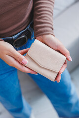 A beautiful woman holds a beige leather purse in her hands. Small women's handbag
