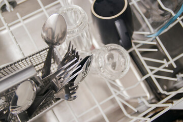 Open dishwasher with white clean dishes after washing in kitchen.