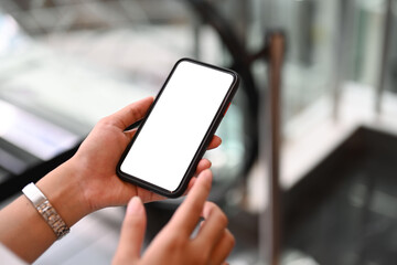 Woman hands typing message on mobile phone while standing on escalator in the shopping mall