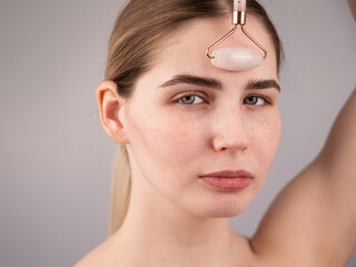 Close-up portrait of a woman uses a quartz roller massager to smooth wrinkles on her forehead.
