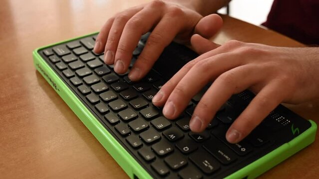 A blind man uses a computer with a Braille display and a computer keyboard. Inclusive device.