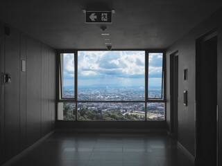 Glass window with cityscape view at hallway in front of lifts in condominium.