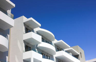 Image of the top of a white building with balconies against a blue sky on a sunny day. Architecture. © Ihor