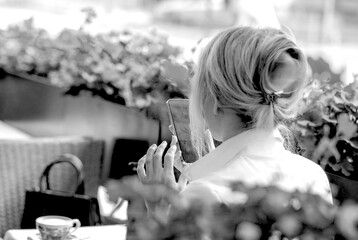 Obraz premium Black and white Banner with a business woman talking on an iphone in a summer cafe. View from the back. Communication concept