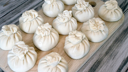 Frozen khinkali are laid out on a wooden board.