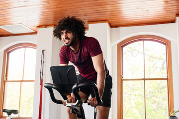 Young middle eastern man doing intense cardio workout on exercise bike at the gym