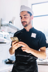 Italian chef with mobile phone in restaurant kitchen