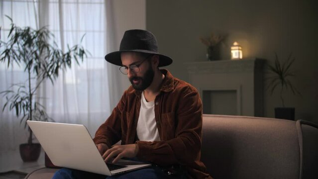 Man working remotely using laptop sitting at couch.Young guy with hat eyeglasses problem manager have an idea.Male thinking about problem solving.