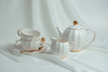 Beautiful white still life with white dishes for tea, coffee, on a white background with silk drapery