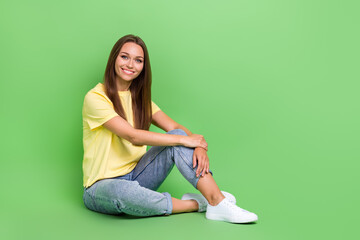 Photo of good looking satisfied person sit floor empty space dressed trendy yellow clothes jeans isolated on green color background