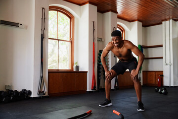 Determined young black man doing squats by battle ropes at the gym