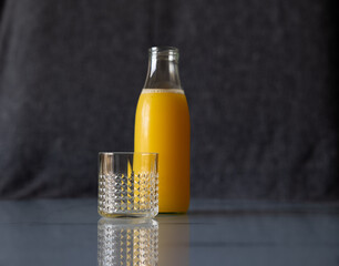 An empty glass on the table against the backdrop of a full bottle of orange juice.