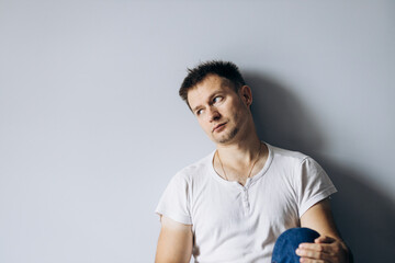 Handsome man in white t-shirt sits on floor thoughtfully sad.