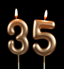 Burning gold birthday candles isolated on black background, number 35