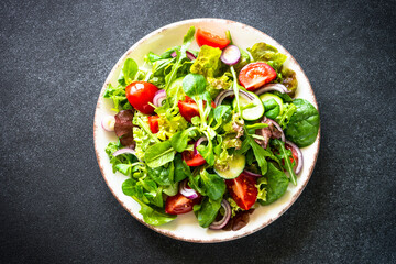 Green salad. Fresh salad leaves and vegetables in white plate at black table. Top view image with copy space.