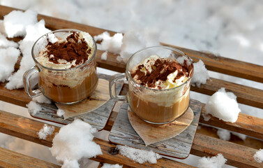 two cups of cappuccino placed on a wooden sled in the  snow