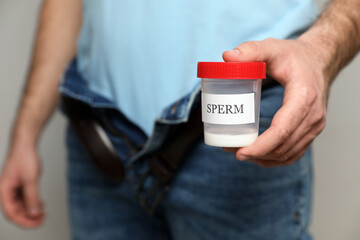 Donor with unzipped pants holding container of sperm, closeup