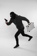 Man wearing black balaclava with metal briefcase and gun on light grey background