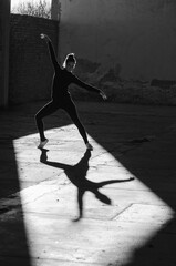 Fototapeta na wymiar Ballerina dancing in an abandoned building on a sunny day in black and white