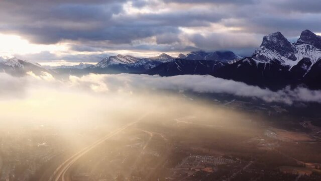 Canmore Alberta mountain range Canadian rockies aerial sunrise drone shot. Dramatic weather, cloudy with a layer of mist moving through the valley.