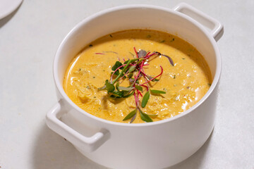 Pumpkin cream soup served with herbs in ceramic pot with lid