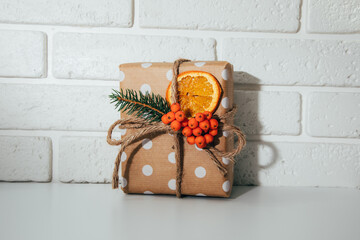 A gift in eco packaging, wrapped in brown paper, decorated with a dry orange and a fir branch. New...