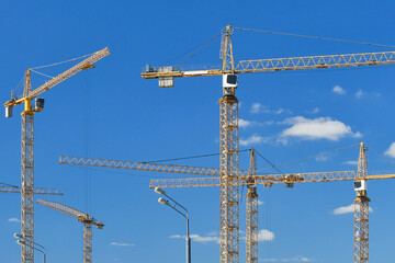 Cranes at construction site. Large construction site, cranes. Tower cranes in action on blue sky background. Housing renovation concept. Selective focus