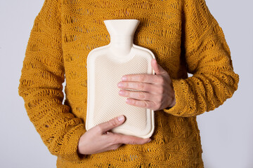 Hot water heating pad is winter essentials.  Power outages and difficulties with heating. Saving electricity. Woman in orange sweater holding heating pad. © Jovana