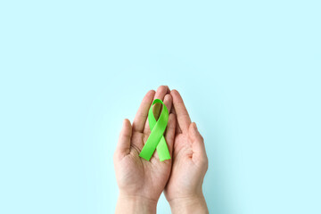 World Mental health awareness day. Woman hands holding green ribbon on blue background.