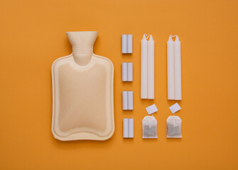 Hot water heating pad, tea bags, candles and batteries are winter essentials on orange background....
