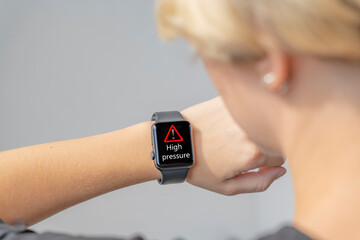 The girl looks at the screen of a black smart watch that shows a signal and a high pressure sign. High blood pressure, Complications after sports. Smart wristwatch. Medical devices.