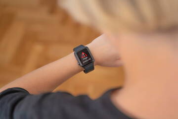 The girl looks at the screen of a black smart watch that shows a signal and a high pressure sign. High blood pressure, Complications after sports. Smart wristwatch. Medical devices.