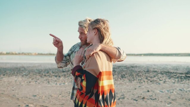 Smiling blond couple pointing finger and walking near estuary outdoors