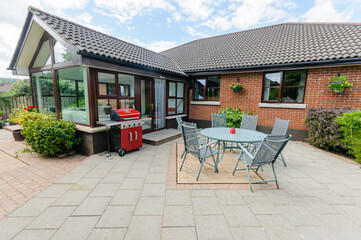 Modern patio with a table, chairs and barbeque behind a bungalow and sunroom.