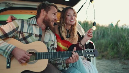 Funny blond young couple playing guitar and singing in the trunk of the car - Powered by Adobe