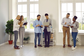 Diverse group of people working in office. Mixed race biracial multiethnic male and female employees and business professionals meet in office workplace, discuss projects and use laptops and tablets