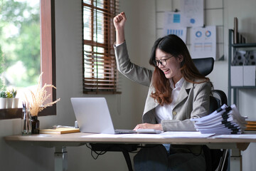 young Asian businesswomen successful excited raised hands rejoicing with a laptop computer in a modern office.