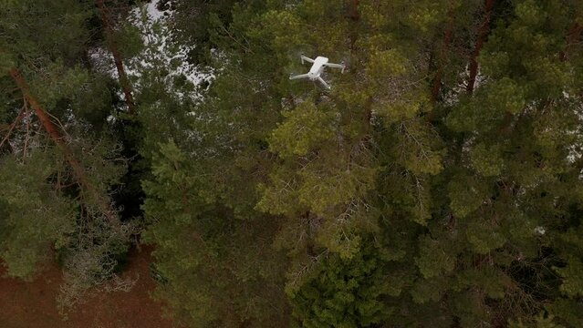 Drone shot from top of another drone flying above snowy forest in rural area, drone spying in air for movement