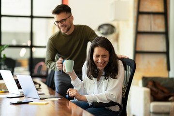 Colleagues laughing in office. Businesswoman and businessman drinking coffee.