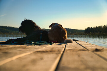 Dog lovers lying on a jetty and looking at the lake in Sweden. Goldendoodle and mix