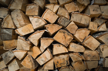 Split birch firewood for heating the home stove and fireplace in winter. Wooden wall from pile of firewood stacked in an shed. Preparation of the stock of firewood for the winter period. Selective