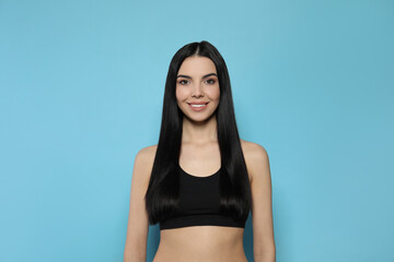 Fototapeta premium Beautiful young woman with long straight hair on light blue background