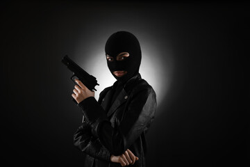 Woman wearing knitted balaclava with gun on black background - obrazy, fototapety, plakaty