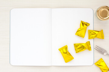 White notebook  and candy on a light wood table