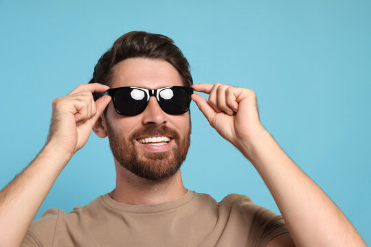 Portrait of smiling bearded man with stylish sunglasses on light blue background, closeup