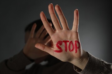 Woman with word Stop written on hand against black background, closeup. Domestic violence concept