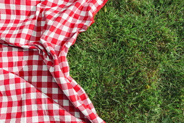 Checkered picnic tablecloth on fresh green grass, top view. Space for text